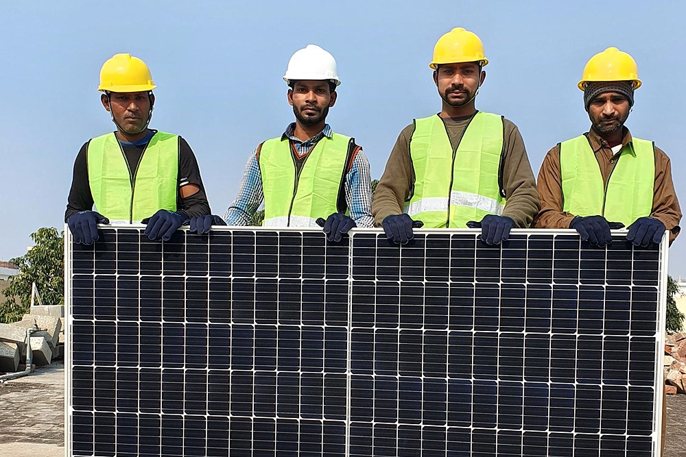 Site crew in hard hats and vests holding a solar module